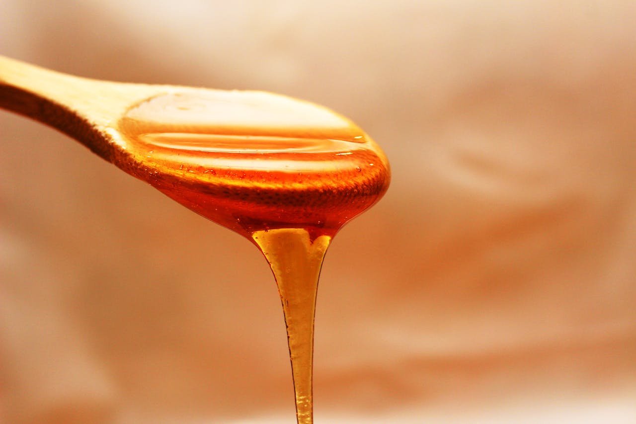 about-us-01 Close-up of honey dripping from a wooden spoon, showcasing its rich texture and color.