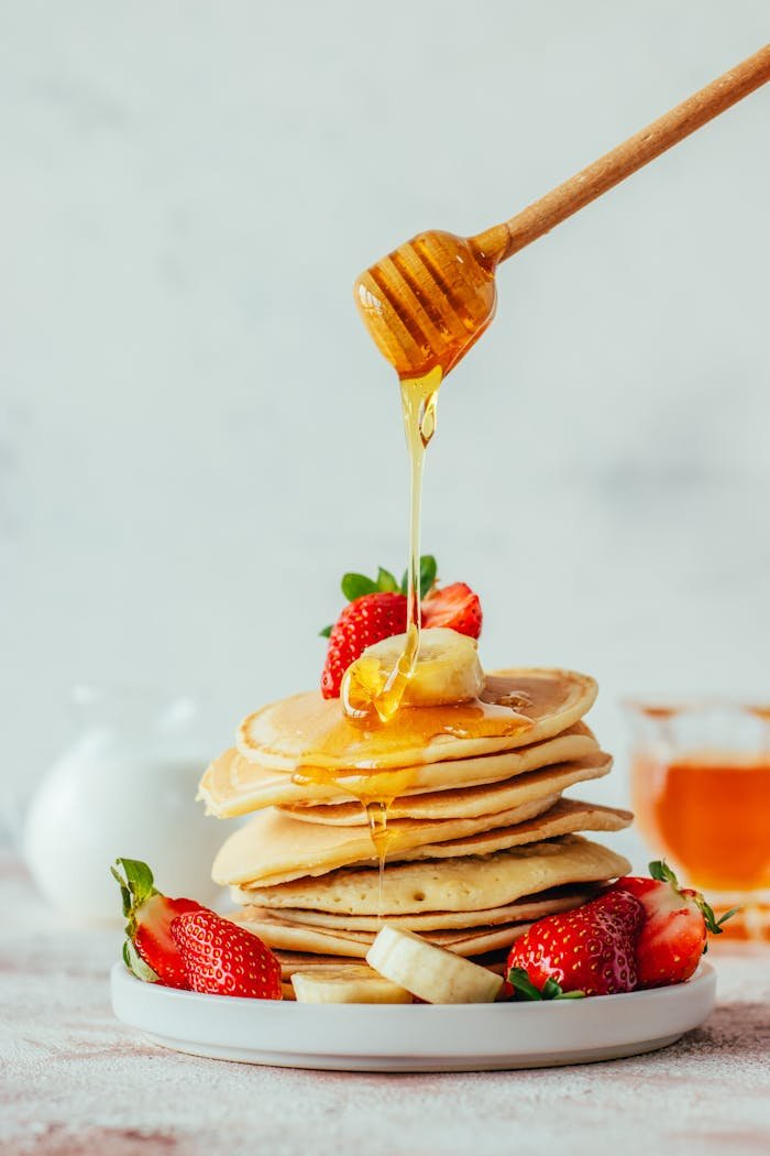 Stack of pancakes topped with fresh strawberries and honey drizzle, perfect for a sweet breakfast.